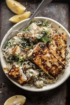 a bowl filled with chicken and rice next to lemon wedges