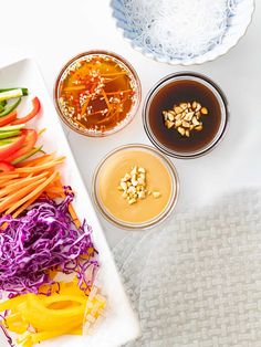 an assortment of vegetables and sauces on a white tablecloth next to two bowls