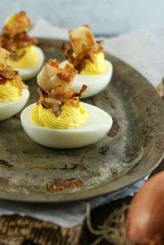 four deviled eggs with bacon on top sit on a metal plate next to an egg shell