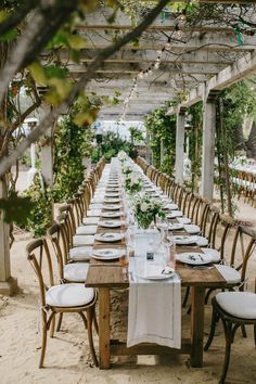 a long table is set with white linens and place settings for an outdoor dinner