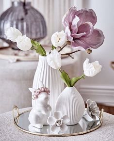 two white vases with flowers in them sitting on a round table next to a mirror