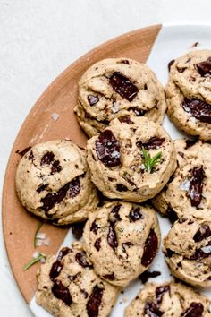 chocolate chip cookies are arranged on a wooden platter with a sprig of rosemary