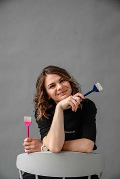 a woman sitting on a chair holding a toothbrush in one hand and smiling at the camera