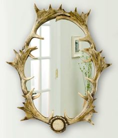 a mirror with antlers on it in front of a white wall next to a potted plant