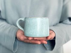 a person holding a blue mug in their hands with both hands on the coffee cup