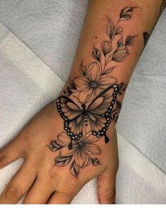 a woman's hand with a butterfly and flowers tattoo on the left side of her wrist