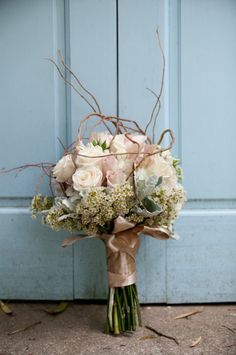 a bouquet of flowers sitting on the ground next to a blue door with brown ribbon