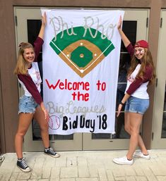 two girls holding up a welcome to the big league banner