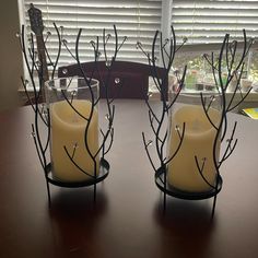 two candles sitting on top of a wooden table next to a glass vase with branches in it