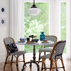 a dining table with four chairs and a vase on the window sill in front of it