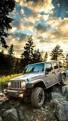 two jeeps are parked on the rocks in front of some trees and bushes at sunset