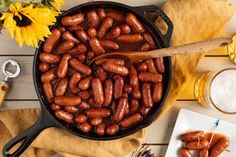 hot dogs are being cooked in a cast iron skillet on a table with sunflowers