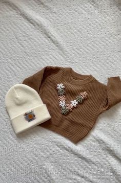 a brown sweater and white hat laying on top of a bed next to each other