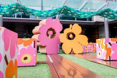 colorful paper flowers are on display in front of a building with green grass and wooden flooring