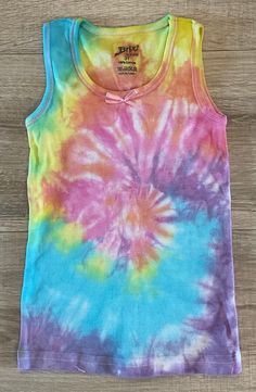 a tie - dyed tank top is sitting on a wooden surface, with the colors of rainbow and blue