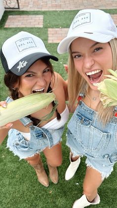 two young women wearing hats and overalls are eating corn on the cob together