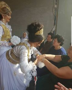 a woman in white dress standing next to another woman wearing a tiara and headpiece