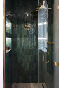 a walk in shower sitting next to a green tiled wall and floor with gold trim