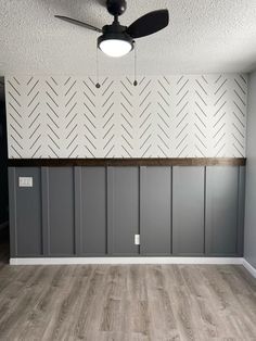 an empty room with gray painted walls and wood flooring on the wall is a ceiling fan