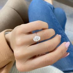 a woman's hand with a diamond ring on her left hand and blue jeans