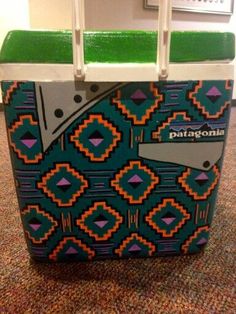 a green and blue cooler bag sitting on top of a carpeted floor next to a wall