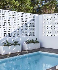 a small pool with two planters next to it and a white fence behind it