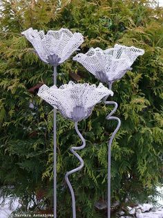 three metal sculptures in the shape of flowers sitting on top of snow covered ground next to a tree