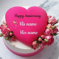 a pink heart shaped cake with flowers on the top and happy anniversary written on it