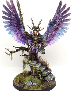 a figurine with purple wings on top of a pile of rocks and trees