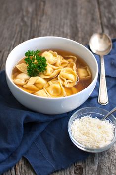 a bowl of soup with noodles and parmesan cheese next to it on a blue napkin