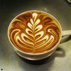 a cappuccino in a white cup on top of a metal countertop