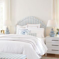 a white bed with blue and white striped pillows