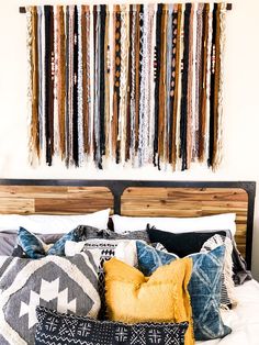 a bed topped with lots of pillows next to a wall hanging on the side of it