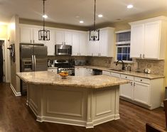 a large kitchen with white cabinets and granite counter tops, an island in the middle