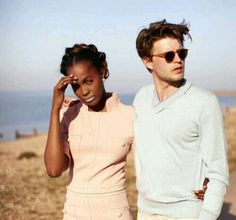 a man and woman standing next to each other on the beach with water in the background