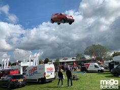 a person flying a red car shaped kite in the air above other cars and trucks