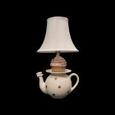 a white teapot with a cupcake on top and a lamp shade over it