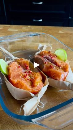 two pieces of salmon in a glass dish with limes and seasoning on the side