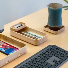 a wooden desk with a keyboard, cell phone and pen holder on the table next to it