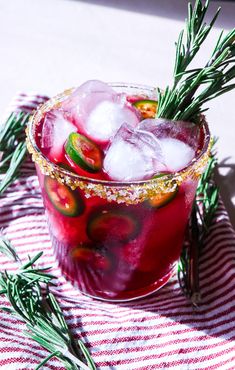 a red drink with ice and rosemary garnish on the rim, sitting on a striped table cloth