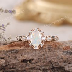 an opal and diamond ring sits on top of a piece of drift wood next to flowers