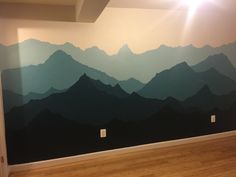 an empty room with mountains painted on the wall and hard wood flooring in front of it