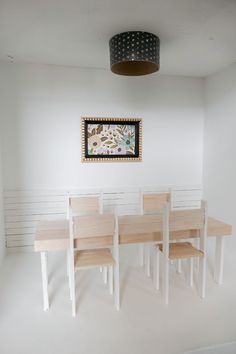 a dining table and four chairs in a room with a painting hanging on the wall