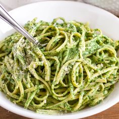 a white bowl filled with pesto pasta next to some spinach and parmesan cheese