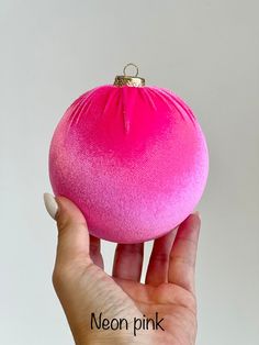 a hand holding a pink ornament in front of a white background with the words neon pink on it