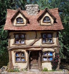 a small house made out of wood and stone with windows on the roof, surrounded by greenery