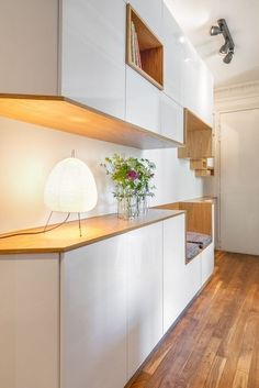 a vase with flowers sitting on top of a counter next to a lamp and cabinets