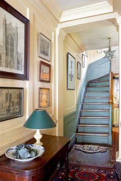 an entry way with stairs and pictures on the wall, along with a blue lamp