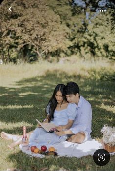 a man and woman are sitting on the grass with an open book in their hands