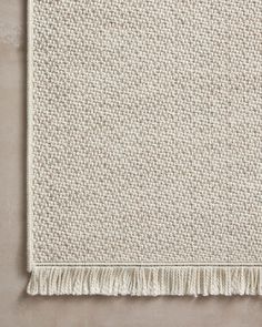 a white rug with fringes on the bottom and one end in beige, against a gray background